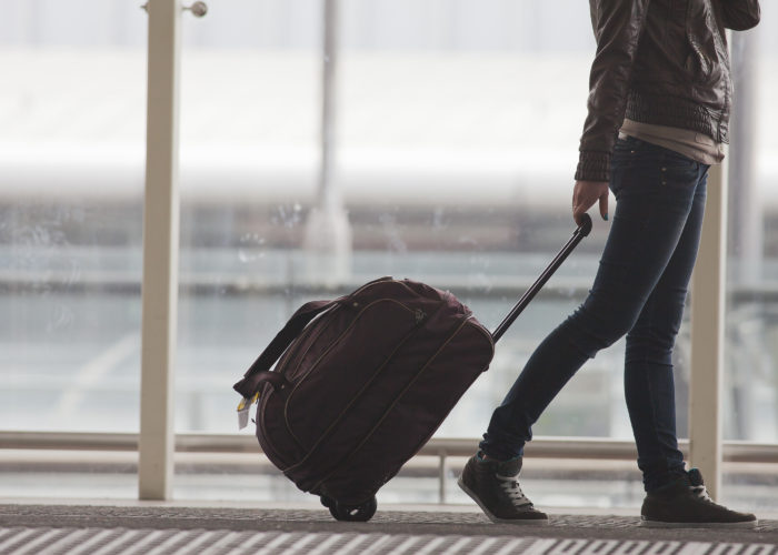 Person rolling a rolling suitcase through an airport hallway