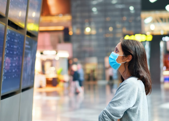 Woman in face mask looking at information board checking her flight in international airport