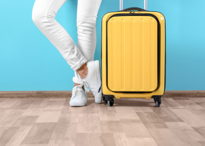Person in white pants standing next to a yellow suitcase in front of a blue wall