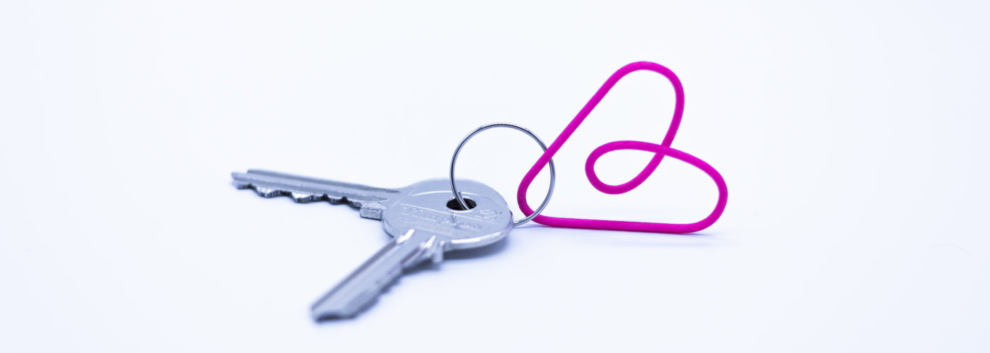 Two house keys attached with a pink paper clip on a white background