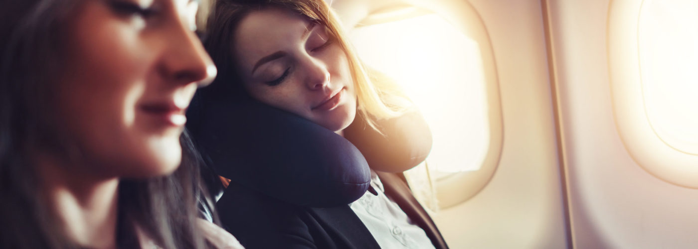 Woman sleeping using a neck pillow in a window seat on an airplane