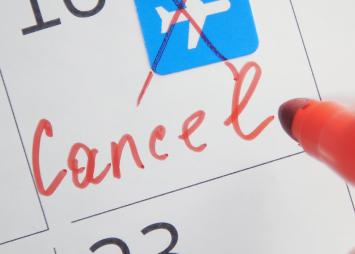Person crossing out a flight emoji in red pen and writing "cancel" below it on a calendar