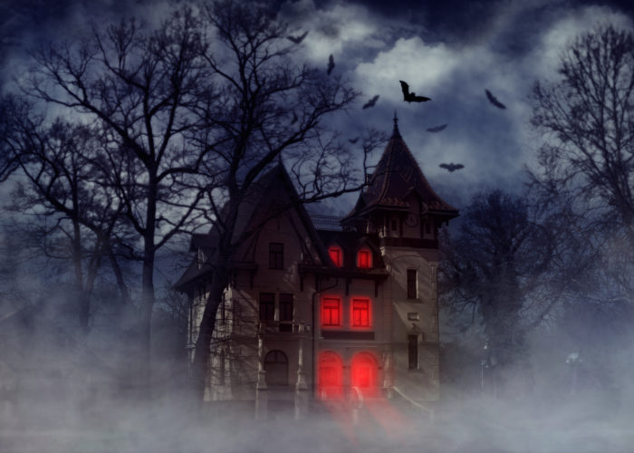 Haunted house on a hill with red lights shining inside and bats flying overhead