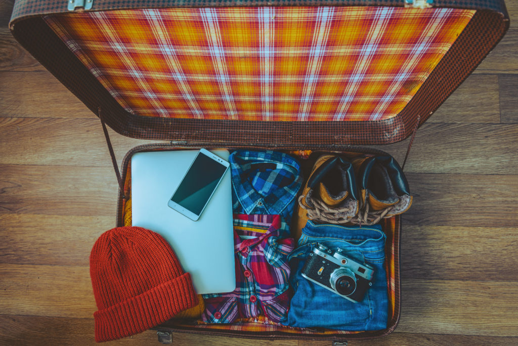 Open suitcase with laptop, phone, shoes, and clothes