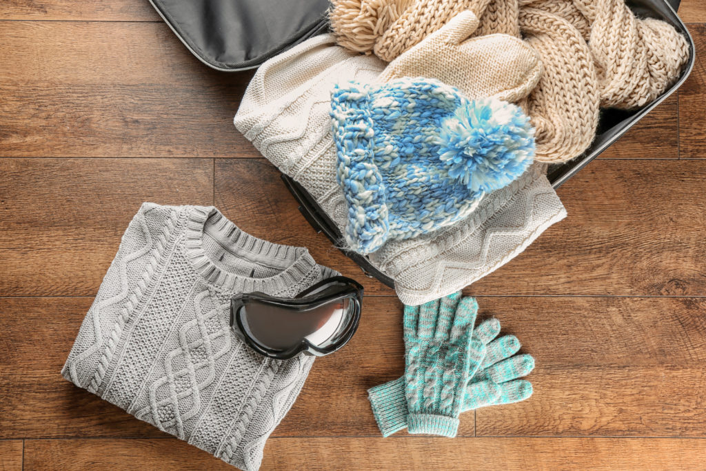 An open suitcase full of winter clothes on a wood floor backdrop