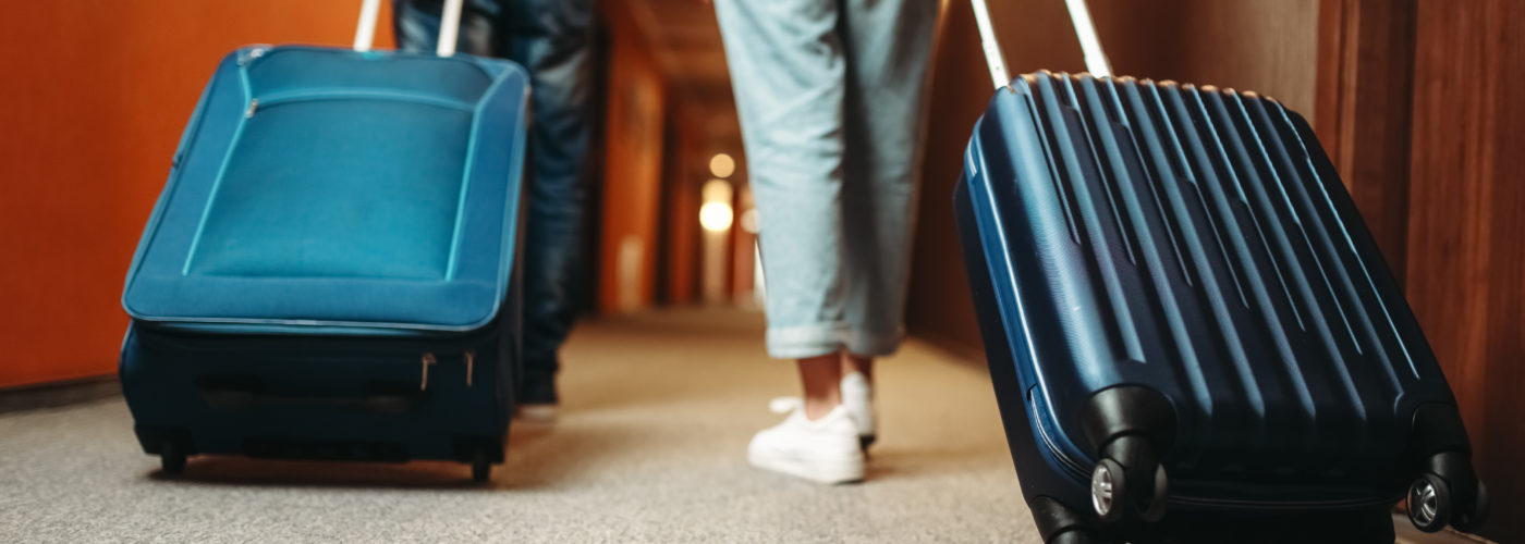 Two people wheeling rolling suitcases down a hotel hallway