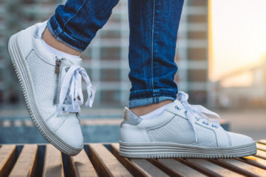 Woman wearing white sneakers walking in city at sunset