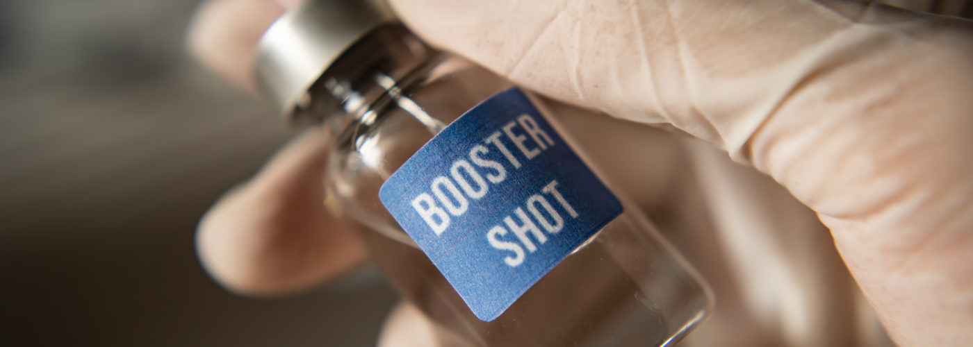 Person drawing COVID-19 vaccine from vial labeled Booster Shot
