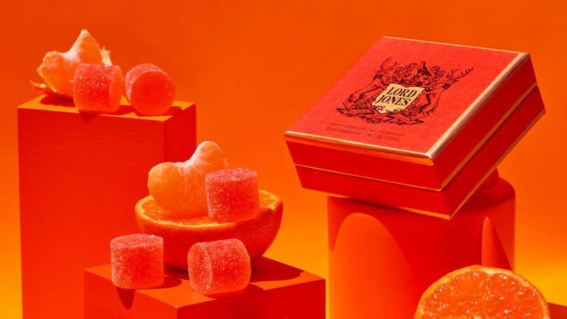 A box of Lord Jones CBD Gumdrops and a few loose drops on an orange backdrop